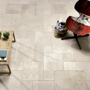 Aerial view of a minimalist room with beige stone tiles. Features a rustic wooden table with two small plants, and a red, distressed chair on a swivel base.
