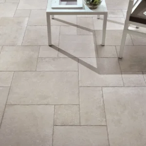 Close-up of a beige tiled patio with a white table and cushioned chair. A magazine lies open on the chair, suggesting a relaxed, inviting atmosphere.