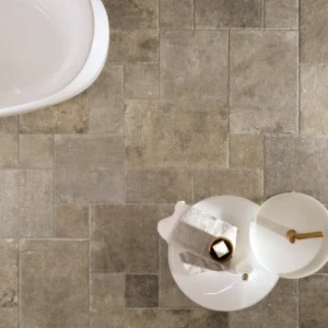Marble beige tiles form a bathroom floor, partially visible. A white side table holds a towel and small items, next to a bathtub corner. Minimalist and serene.